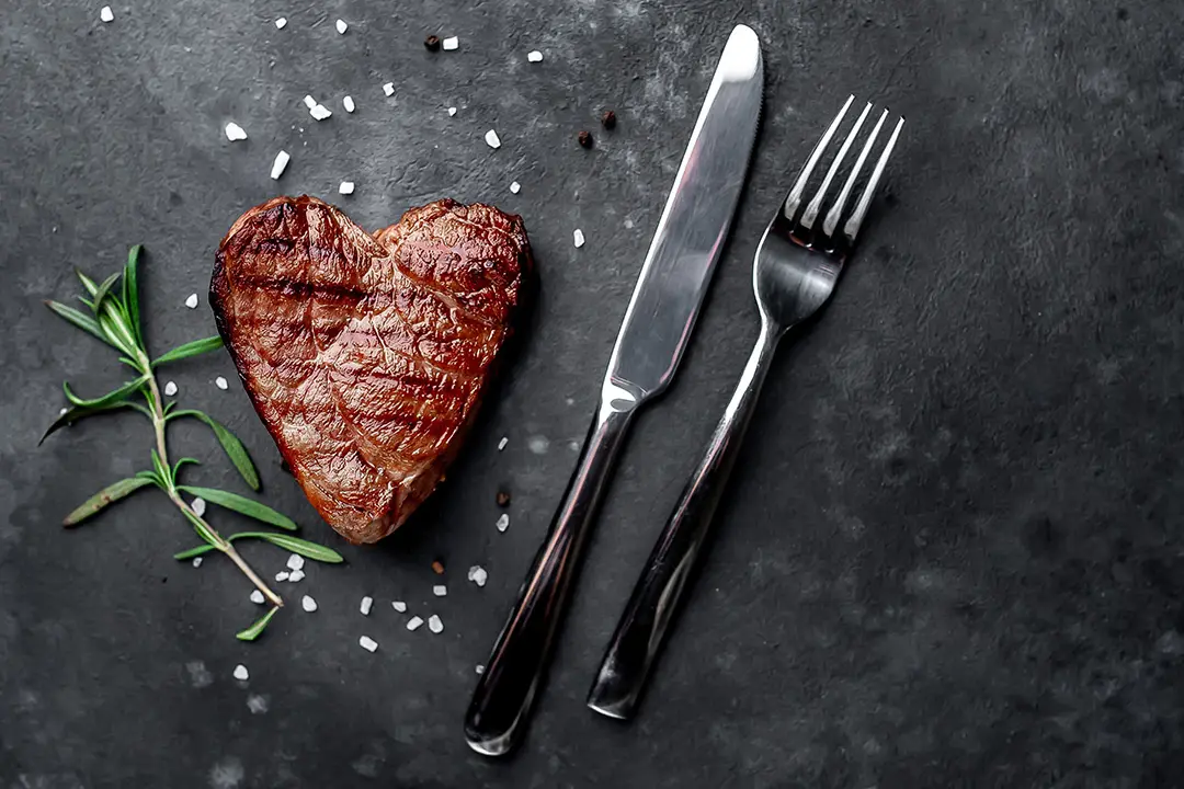 Steak in Herzform neben Messer und Gabel